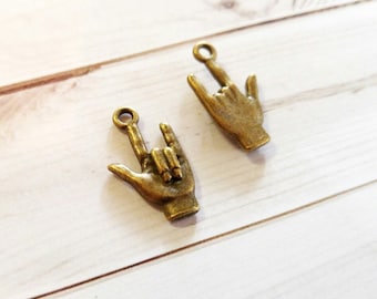 Puede incluir: Dos abalorios de metal dorado en forma de manos haciendo el signo de la lengua de señas americana para "Te amo".