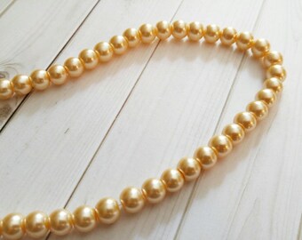 May include: A strand of golden pearl beads on a white wooden surface.