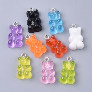 May include: Ten gummy bear charms in a variety of colours, including purple, blue, orange, red, green, yellow, pink, white, and black. The charms are made of resin and have a shiny finish. They are ideal for adding a fun and playful touch to jewellery, keyrings, and other crafts.