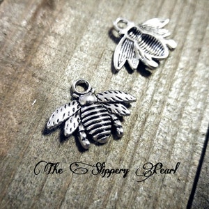 May include: Two silver bee charms with detailed wings and a striped body. The charms have a loop at the top for attaching to jewelry or other crafts.
