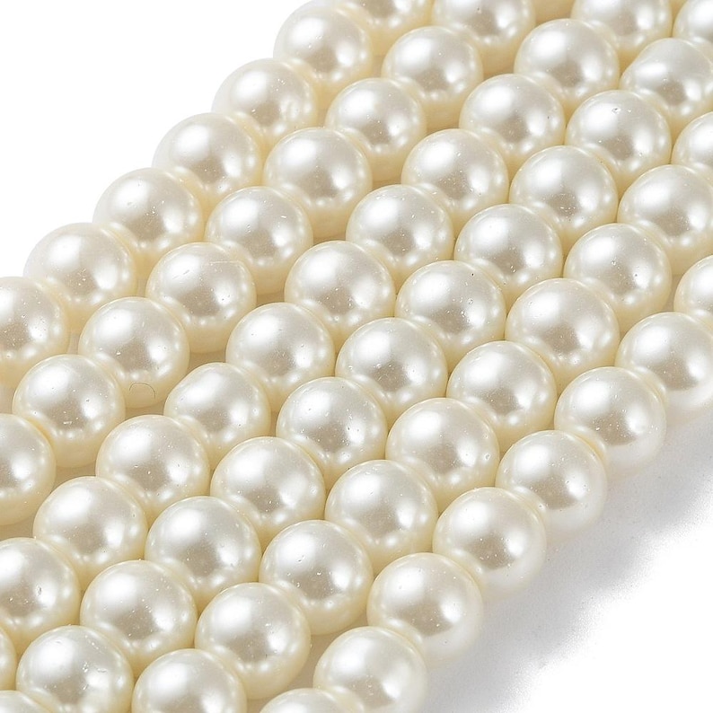 May include: Close-up of multiple strands of creamy white, round pearls. The pearls are arranged in diagonal rows, showcasing their smooth, lustrous surface. The image highlights the consistent size and color of the pearls, suggesting they are uniform in quality.