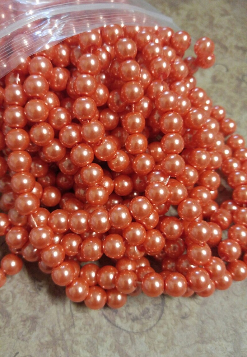 May include: Strands of orange-colored faux pearls, tightly strung together. The pearls have a glossy finish and are clustered together, creating a full and textured appearance. The beads are a warm, inviting color, suitable for jewelry making or craft projects.