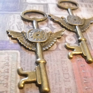 May include: Two antique-style brass keys with wings and a clock face design. The keys have a worn, aged look and are perfect for crafting or decorating.