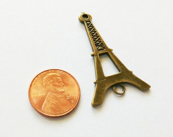 May include: A bronze-colored Eiffel Tower charm with a penny for scale. The charm is a miniature replica of the famous Parisian landmark, featuring intricate lattice detailing. The penny is dated 2017.