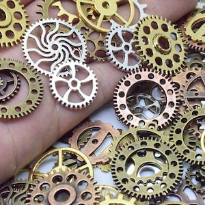 Op de afbeelding: Een verzameling van verschillende metalen tandwielen in verschillende maten en afwerkingen, waaronder goud, zilver en koper. De tandwielen zijn op een hand gerangschikt, waardoor een steampunk-esthetiek ontstaat.
