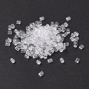 May include: A large pile of clear plastic earring backs. The backs are small and cylindrical in shape.