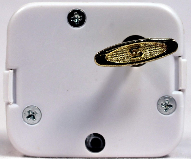 May include: White music box with a gold-colored winding key. The key is shaped like an oval with a textured surface. There are four screws on the box.