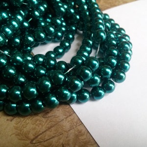 May include: A strand of teal green pearl beads. The beads are round and have a high gloss finish.