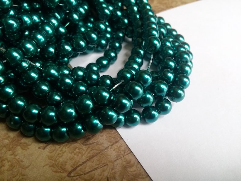 May include: A strand of teal green pearl beads. The beads are round and have a high gloss finish.