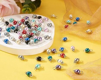 May include: Assortment of colourful pearl beads with silver caps. The beads are arranged on a white plate and scattered on a yellow surface.