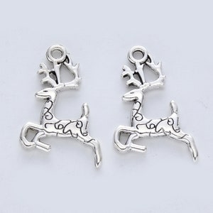 May include: Two silver reindeer charms with intricate details. The reindeer are in a running pose with their antlers raised. The charms have a loop at the top for attaching to jewelry or other crafts.