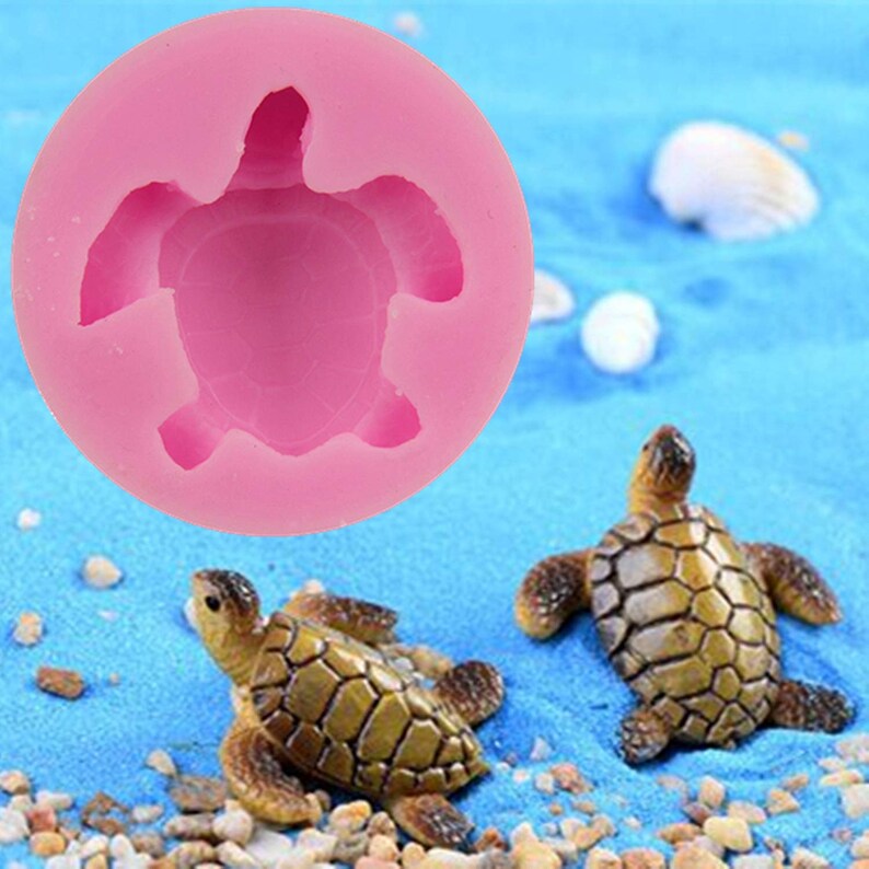 May include: Pink silicone mold shaped like a turtle. Two small turtle figurines are shown on a blue surface.