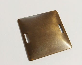 May include: A square, bronze-colored metal plate with rounded corners and two rectangular cutouts. The plate has a brushed texture and a slightly reflective surface, suggesting a vintage or industrial aesthetic.
