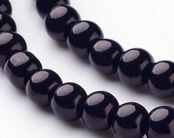 Puede incluir: Primer plano de un collar de cuentas negras brillantes. Las cuentas son esféricas y de tamaño uniforme, reflejando la luz. El fondo es blanco suave, resaltando las cuentas oscuras. La imagen sugiere joyería o suministros para manualidades.