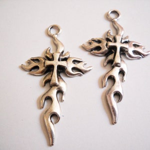 May include: Two silver-toned metal cross charms with a flame design. The crosses have a simple, traditional shape and are surrounded by stylised flames.