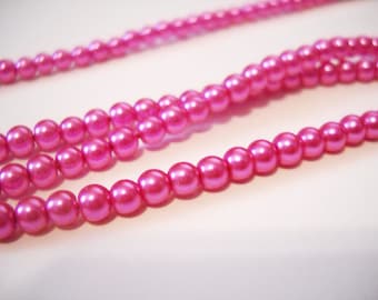 May include: Close-up of several strands of pink beads. The beads are small, round, and have a glossy finish. The strands are arranged in a slightly curved pattern, with some strands in the background out of focus. The beads are a vibrant shade of pink.