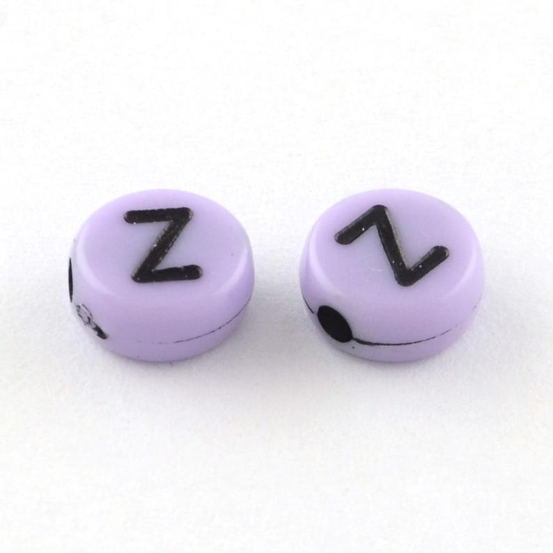 K&ouml;nnte beinhalten: Zwei lila Buchstabenperlen mit dem Buchstaben "Z" in Schwarz auf jeder Perle.