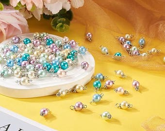 May include: Assortment of pastel coloured pearl beads with silver accents. The beads are arranged on a white plate and scattered on a yellow surface.