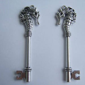 May include: Two silver-toned key charms shaped like seahorses. The charms have intricate details and a vintage style.