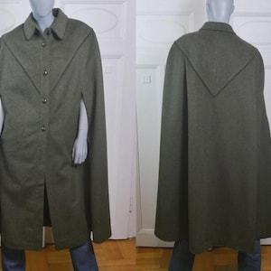 May include: An olive green wool cape coat with a button-up front and a collar. The cape has arm slits and a decorative design on the back. The coat is displayed on a mannequin.