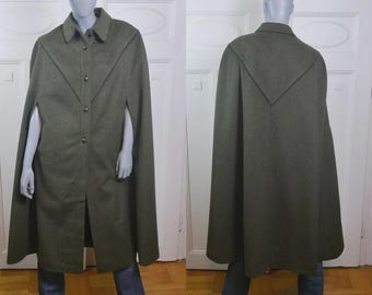 Könnte beinhalten: Ein olivgrüner Woll-Cape-Mantel im Vintage-Stil mit Knopfleiste und Kragen. Der Cape hat Armausschnitte und ein dekoratives Design auf der Rückseite. Der Mantel wird auf einer Schaufensterpuppe präsentiert.