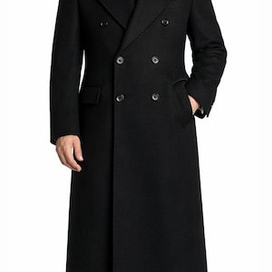 May include: A black double-breasted overcoat with a notched lapel, worn over a white dress shirt and black tie. The coat has a long length, reaching the ankles, and features two rows of buttons. The model is wearing black dress pants and shoes.