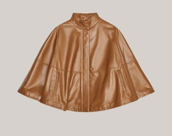May include: A brown leather cape with a high collar and a button closure. The cape has a smooth, shiny finish and a tailored design. The garment features two small pockets on the front. The cape is a stylish outerwear piece.