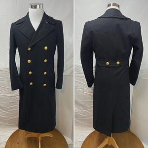 May include: A black double-breasted coat with gold-colored buttons. The coat has a long length and a classic design. The coat is displayed on a mannequin, showcasing the front and back views. The coat is made of a dark fabric.