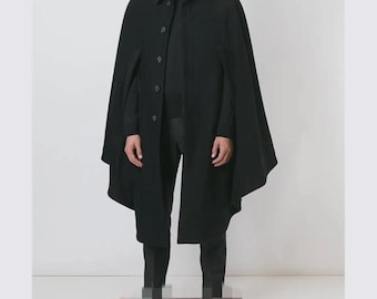 May include: A black cape coat with a button-up front and a collared neckline. The coat is worn over a black outfit, creating a monochromatic look. The cape has a flowing design.