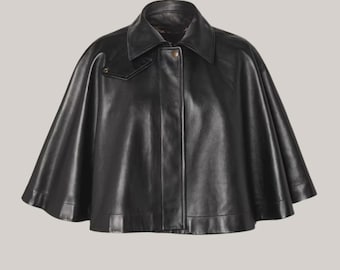 May include: A black leather cape with a collar and a single button closure. The cape has a classic design with a smooth, shiny finish. The garment is a stylish outerwear piece.