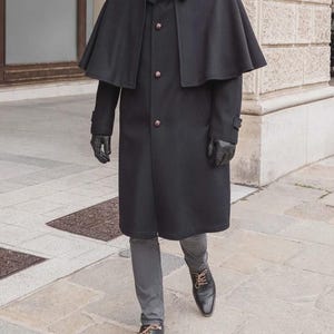 May include: A black wool cape coat with a button-up front and a short cape overlay. The coat features a classic design with a high collar and is paired with black gloves and dress shoes. The coat is a stylish outerwear option.