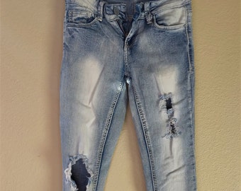 May include: Light blue denim jeans with distressed details and the text "Vanilla Star" on the waistband.