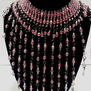 Pode incluir: Um colar de contas de cristal rosa com uma parte superior estilo choker e longos fios de contas pendurados.