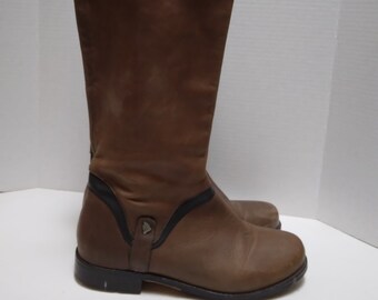 May include: Brown leather riding boots with black accents and a zipper on the back. The boots have a low heel and a rounded toe.