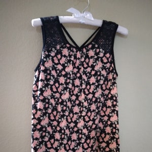 May include: A sleeveless black and pink floral print top with a lace overlay on the shoulders. The top has a criss-cross back.