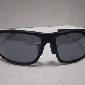 May include: Black sunglasses with gray lenses. The sunglasses have a thick, curved frame and a sporty design. The lenses are reflective, and the sunglasses appear to be made of a durable material. The overall style is modern and suitable for outdoor activities.