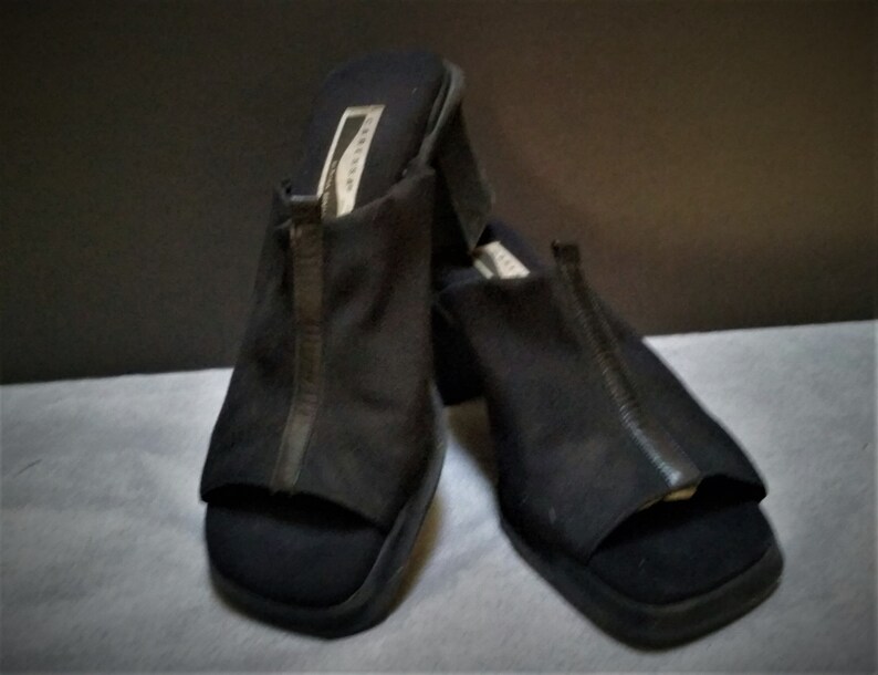 Puede incluir: Un par de sandalias negras de tac&oacute;n con abertura en la punta y un detalle de cremallera en la parte delantera. Las sandalias tienen un tac&oacute;n grueso y est&aacute;n hechas de un tejido suave y texturizado.