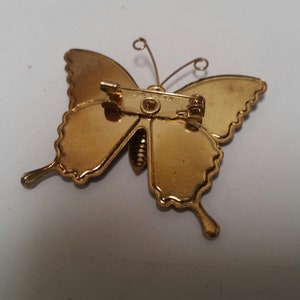 May include: Gold-toned butterfly brooch with a pin closure. The butterfly has a detailed design and a textured finish.