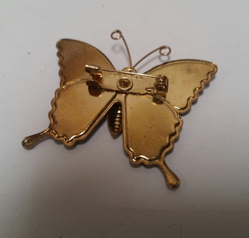 May include: Gold-toned butterfly brooch with a pin closure. The butterfly has a detailed design and a textured finish.