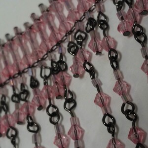 Pode incluir: Franja de contas rosa e preta com uma corrente e elos em forma de cora&ccedil;&atilde;o. A franja &eacute; feita de pequenas contas facetadas.