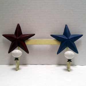 May include: A yellow metal coat rack with two star-shaped hooks. The stars are painted red and blue with white ceramic knobs.