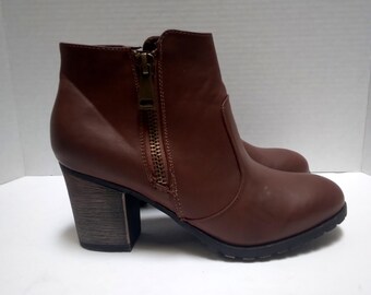 May include: Brown ankle boots with a side zipper and a block heel. The boots have a smooth, leather-like appearance and a dark brown sole. The heel has a wood-grain texture.