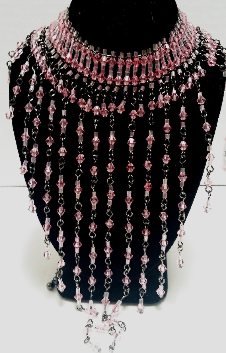 Pode incluir: Um colar de contas de cristal rosa com uma parte superior estilo choker e longos fios de contas pendurados.