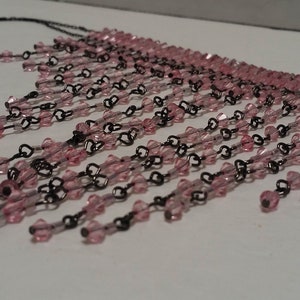Pode incluir: Um colar de contas rosa e preto com um design de franja. O colar &eacute; feito de pequenas contas rosa enfiadas em uma corrente preta.