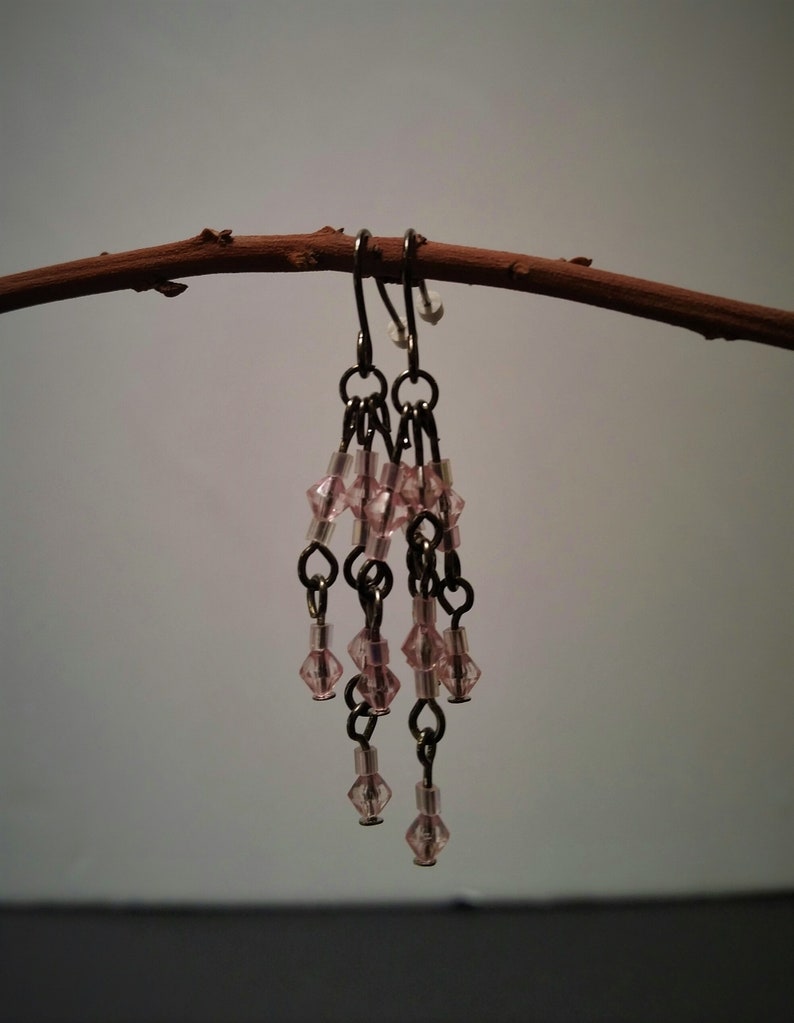 Pode incluir: Um par de brincos pendentes com contas de vidro rosa e correntes prateadas.