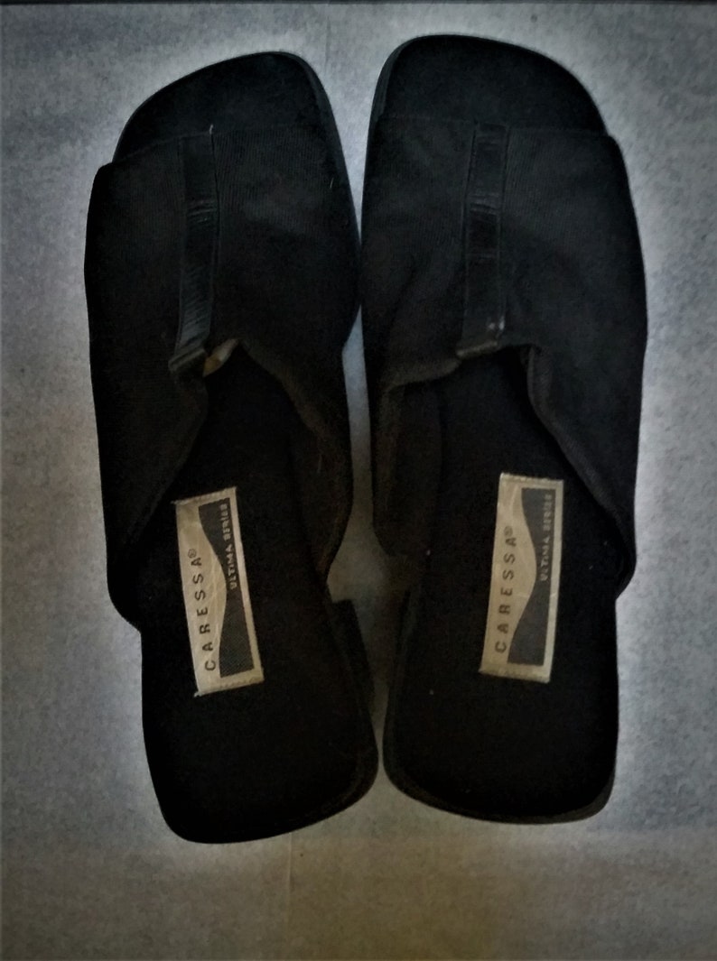 Puede incluir: Un par de sandalias negras de vestir con una correa en la parte superior. Las sandalias tienen una etiqueta en el interior que dice "Carressa&reg; Ultima Series".