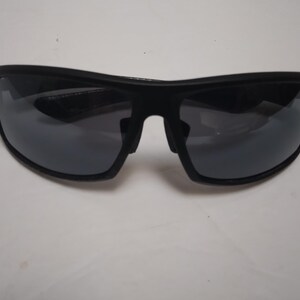 May include: Black sunglasses with dark gray lenses. The sunglasses have a curved, sporty design with a thick frame. The lenses are reflective, and the overall look is sleek and modern. Suitable for outdoor activities.