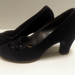 May include: A pair of black vintage heels. These shoes feature a rounded toe, a cut-out design on the vamp, and a chunky heel. The heels are approximately 2.5 inches (6.35 cm) high, and the shoes appear to be made of a soft, velvety material.