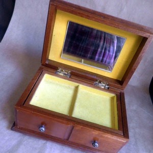 May include: A wooden jewelry box with a hinged lid and two small drawers. The interior is lined with yellow fabric and includes a small mirror. The box is made of dark wood and has silver-colored drawer pulls.