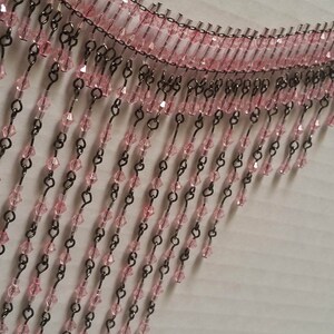 Pode incluir: Uma guarni&ccedil;&atilde;o de franja de contas cor-de-rosa com elos de corrente de metal preto. A franja &eacute; feita de pequenas contas facetadas que pendem da corrente.
